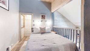 A bedroom with a bed, a nightstand, a wall-mounted light, a door, and a balcony with a railing. - Mountain studio & loft with fireplace, near skiing & trails (Sun Valley)