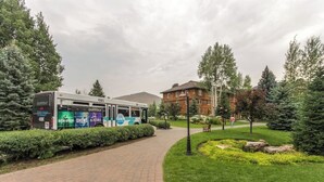 A paved pathway leading to a bus stop with a bus, surrounded by greenery and a building with a red roof. - Mountain studio & loft with fireplace, near skiing & trails (Sun Valley)