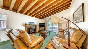 Una sala de estar acogedora con chimenea, sofás de cuero, televisor y un amplio ventanal.