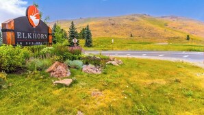 Letrero de 'Elkhorn in Sun Valley' con un logotipo de ciervo, rodeado de follaje y una carretera.