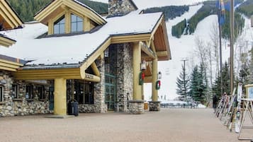 Una cabaña de paredes de piedra, techo cubierto de nieve y un telesilla al fondo.