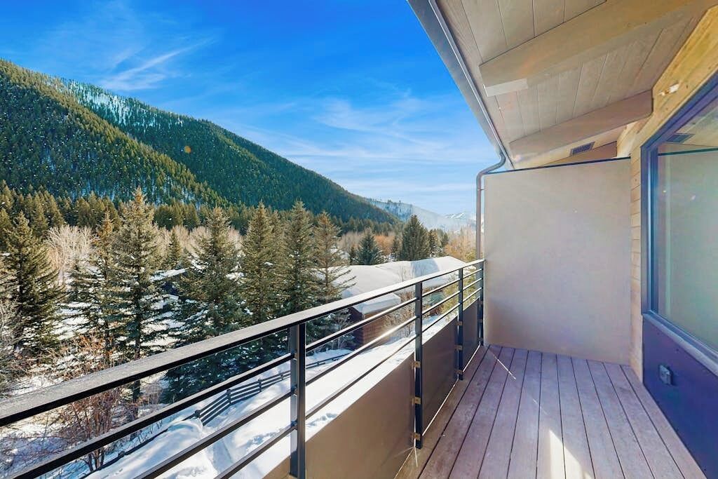Un balcón con vistas a una montaña arbolada y terreno cubierto de nieve.