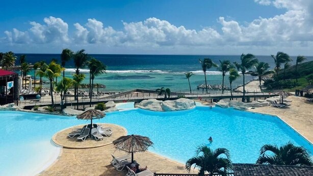 Ein Pool im Resort mit Blick auf den Ozean, Palmen und einen Strand.