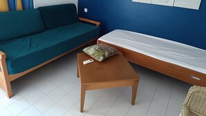 Ein Zimmer mit einem grünen Sofa, einem Holztisch mit einer Fernbedienung und einer weißen Matratze an einer blauen Wand.