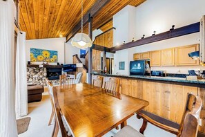 A wooden dining table with chairs, a kitchen with wooden cabinets, a stone wall, and a painting of sunflowers. - Charming condo with mountain views, fireplace, hot tub & deck (Ketchum)
