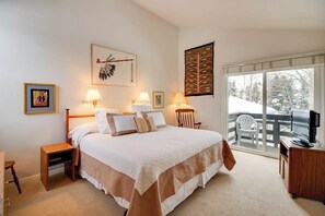 A bedroom with a large bed, two bedside tables, a chair, a desk, a television, and a balcony with a view of trees. - Cozy Condo w/ Free WiFi, Heated Pool & Tennis - Close to Skiing (Sun Valley)