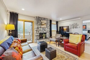 Ein Wohnzimmer mit Kamin aus Stein, einer Couch, einem roten Sessel und einem Fernseher.