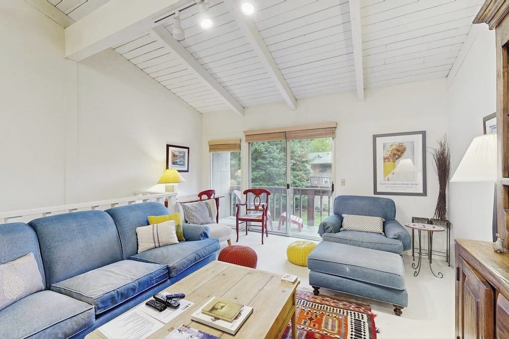 A living room with a blue sofa, a wooden coffee table, and a balcony with a view.