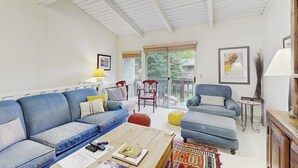 Ein Wohnzimmer mit einem blauen Sofa, einem Holztisch und einem Balkon mit Blick.