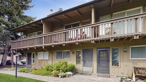Ein zweistöckiges Gebäude mit Balkon, mehreren Türen und einem kleinen Garten.