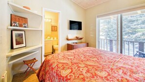 A bedroom with a large bed, a TV, a bookshelf, and a view of trees through the window. - Cozy Mountain Abode with WiFi, Pool, & Perfect Location Near Downtown Ketchum (Sun Valley)