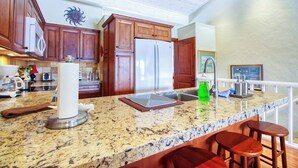 A kitchen with wooden cabinets, a granite countertop, a stainless steel refrigerator, and a bar area with stools. - Cozy Mountain Abode with WiFi, Pool, & Perfect Location Near Downtown Ketchum (Sun Valley)