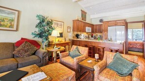 A cozy living room with a sofa, armchairs, a coffee table, and a dining area with a kitchen in the background. - Cozy Mountain Abode with WiFi, Pool, & Perfect Location Near Downtown Ketchum (Sun Valley)