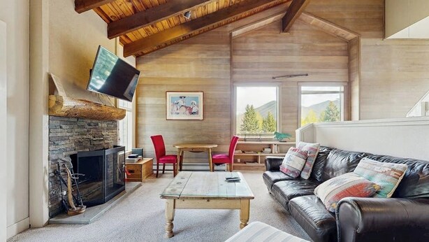 Ein Wohnzimmer mit Kamin aus Stein, einem flachbildfernseher an der Wand, einem Ledersofa und einem Holztisch.