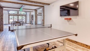 Ein Tischtennis-Tisch in einem Raum mit einem an der Wand montierten Fernseher und einem Fluchtzeichen über einer Tür.