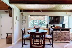 A dining area with a round table, two chairs, a wooden cabinet, and a window with a view of trees. - Cute Studio with Lots of Space, WiFi, Close to Skiing (Sun Valley)