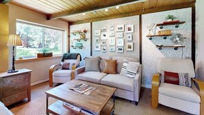 Ein gemütliches Wohnzimmer mit einer Couch, einem Sessel, einem Couchtisch und an der Wand befestigten Regalen mit Bildern.