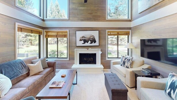 Un salón amplio con chimenea, ventanas grandes y un ventilador de techo.