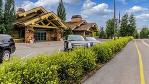 Una cabaña con fachada de piedra, un porche cubierto y un estacionamiento con coches.