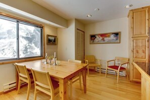 Un coin repas avec une table et des chaises en bois, une fenêtre donnant sur des arbres et un tableau accroché au mur.