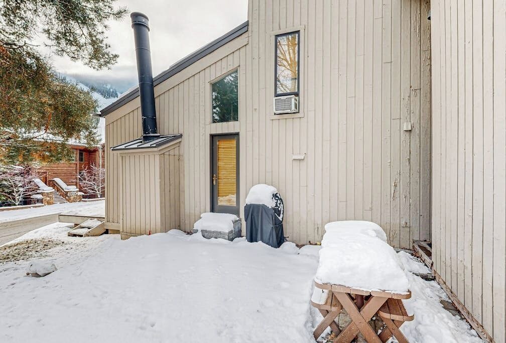 A wooden building with a chimney, a covered bench, and a snow-covered ground.