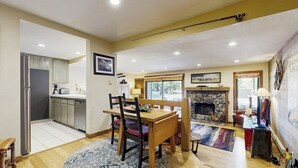 Ein geräumiges Wohnzimmer mit Kamin, eine Essecke mit Holztisch und Stühlen sowie eine Küche mit modernen Geräten.