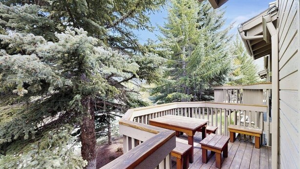 A wooden deck with benches and a railing, surrounded by evergreen trees. - Rustic home with gas fireplace, pool & hot tub - ski-in/out to Dollar Mountain (Sun Valley)