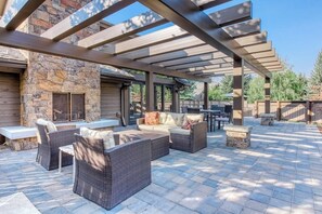 An outdoor patio with wicker furniture, a stone fireplace, and a pergola structure. - Ski-in/ski-out alpine condo with prime location, shared pool, hot tub, & tennis (Sun Valley)
