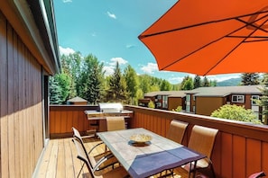 A wooden deck with a table and chairs, a grill, and an umbrella. - Thoughtfully renovated condo with Sun Valley pass to pool & tennis (Sun Valley)