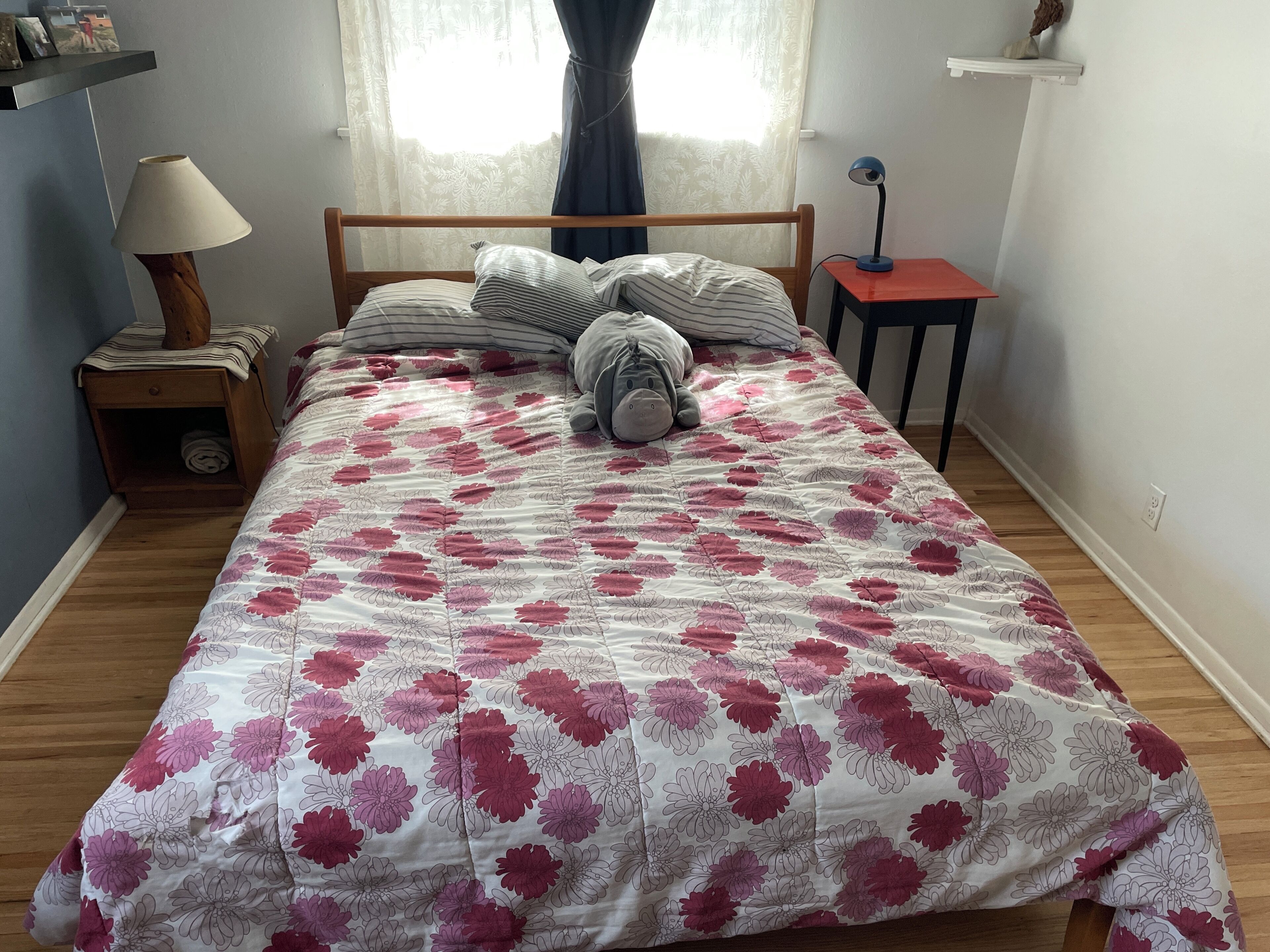 Ein Schlafzimmer mit einem blumigen Bettüberwurf, einem Holz-Kopfteil, einer Nachttischlampe, einem Nachttisch und einem kleinen Tisch mit einer Lampe.