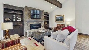 Ein Wohnzimmer mit Kamin aus Stein, einem darüber montierten Fernseher, einer Couch, einem gemusterten Teppich und einem Holztisch.