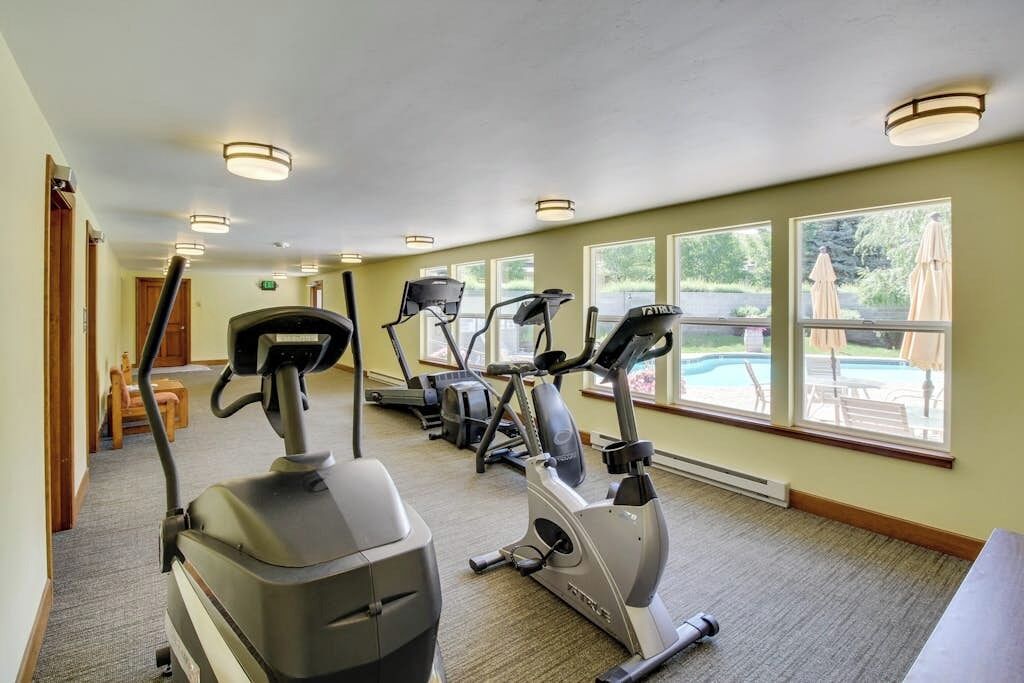 A gym with stationary bikes, treadmills, and a pool view.