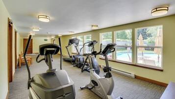 A gym with stationary bikes, treadmills, and a pool view.