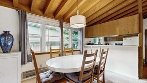 Un coin repas avec une table ronde et des chaises en bois, un plafond blanc et une cuisine en arrière-plan.