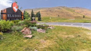 Une enseigne pour « Elkhorn in Sun Valley », avec un logo représentant un cerf, entourée de verdure et d’une route.