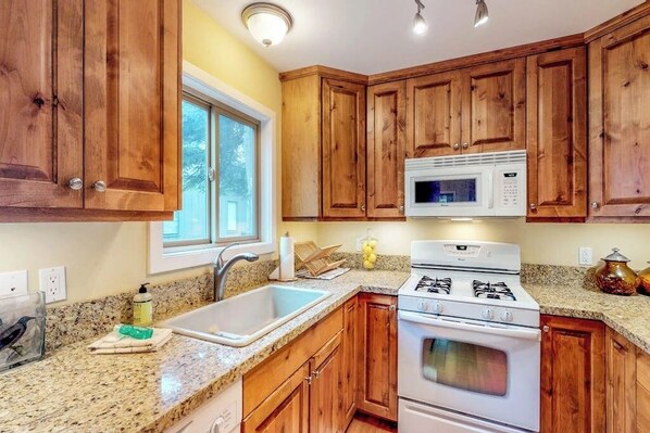 A kitchen with wooden cabinets, a granite countertop, a microwave, a stove, and a sink. - Centrally located condo with mountain views - on bike path (Ketchum)