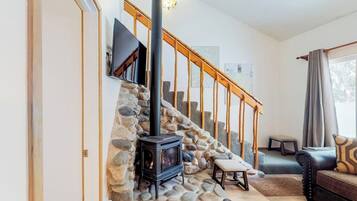 A living room with a stone wall, a fireplace, a staircase, and a sofa.