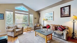Un salon avec deux canapés, une table basse et un lampadaire. De grandes fenêtres et un tableau encadré ornent le mur.