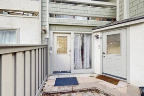 Ein schmaler Gang mit einer weißen Tür, einer blauen Fußmatte und einem kleinen Podest, das zu einer Tür mit Fenster und Rollo führt.