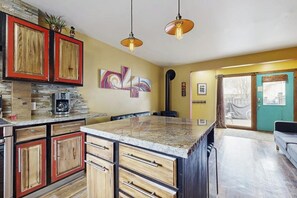 Eine Küche mit Holzausstattung, einer Granit-Arbeitsplatte, Pendelleuchten und einer großen Kochinsel.