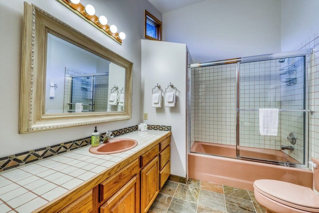 A bathroom with a large mirror, a sink, a toilet, and a glass-enclosed shower.