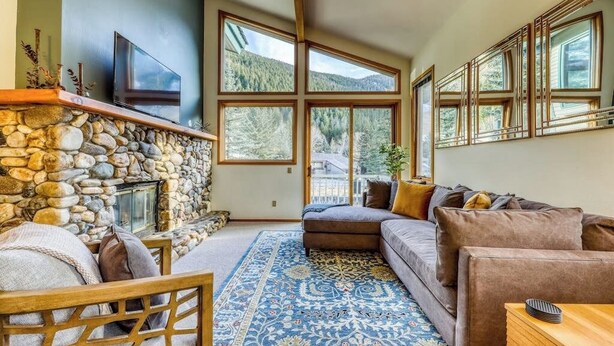 A living room with a stone fireplace, large windows, a sofa, and a TV. - Newly-updated Warm Springs condo w/ski & mountain views - Dogs ok (Ketchum)