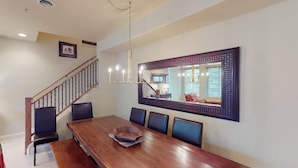 A dining area with a wooden table, six chairs, a chandelier, and a large mirror on the wall. - Comfortable, centrally-located condo close to skiing, hiking, & downtown (Ketchum)
