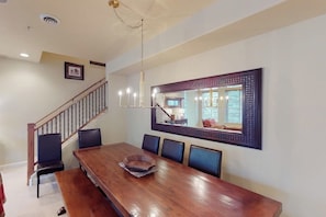 A dining area with a wooden table, six chairs, a chandelier, and a large mirror on the wall. - Comfortable, centrally-located condo close to skiing, hiking, & downtown (Ketchum)
