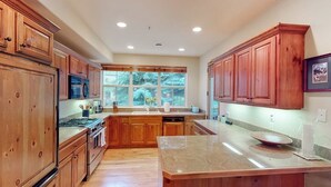 A kitchen with wooden cabinets, a granite countertop, and a window with a view of trees. - Comfortable, centrally-located condo close to skiing, hiking, & downtown (Ketchum)