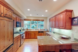 A kitchen with wooden cabinets, a granite countertop, and a window with a view of trees. - Comfortable, centrally-located condo close to skiing, hiking, & downtown (Ketchum)