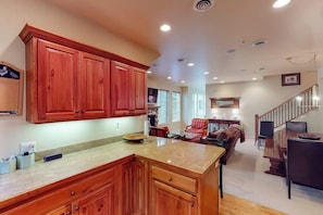 A spacious kitchen with wooden cabinets, a granite countertop, and a dining area with a staircase. - Comfortable, centrally-located condo close to skiing, hiking, & downtown (Ketchum)