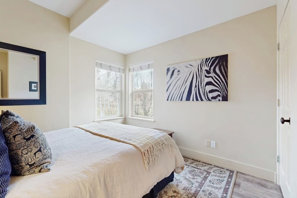 Une chambre à coucher avec un lit, une fenêtre, une œuvre d’art à motifs zébrés et une porte.