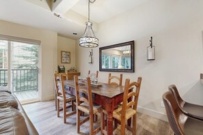 Ein Essbereich mit Holztisch und Stühlen, einer Kandelaberleuchte, einem großen Spiegel und Blick durch ein Fenster.