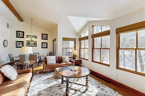 A spacious living room with a fireplace, large windows, and a high ceiling. - Spacious mountain getaway near the slopes with riverfront view & garage (Ketchum Idaho)